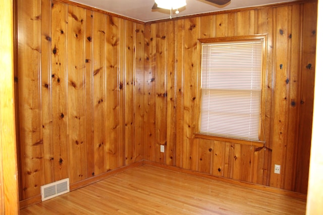 unfurnished room featuring ceiling fan, light wood-style flooring, wood walls, and visible vents