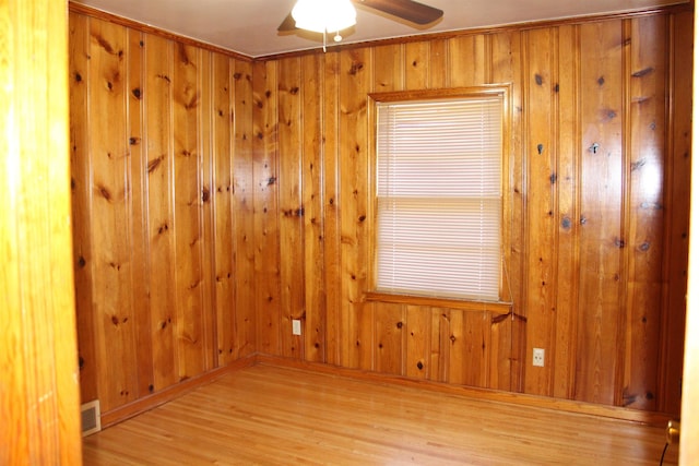 unfurnished room with wooden walls, a ceiling fan, and light wood-style floors