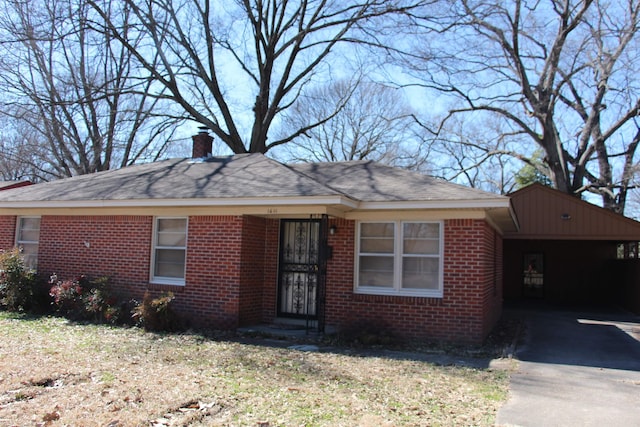 ranch-style house with driveway, brick siding, and a chimney