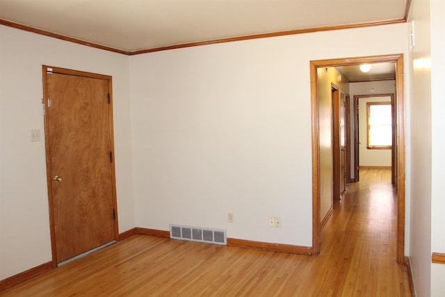 empty room with ornamental molding, visible vents, light wood-style flooring, and baseboards