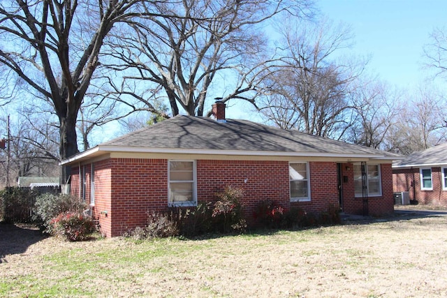 view of side of property with a yard, a chimney, central AC unit, and brick siding