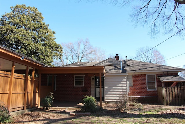 rear view of house featuring a chimney, fence, and brick siding