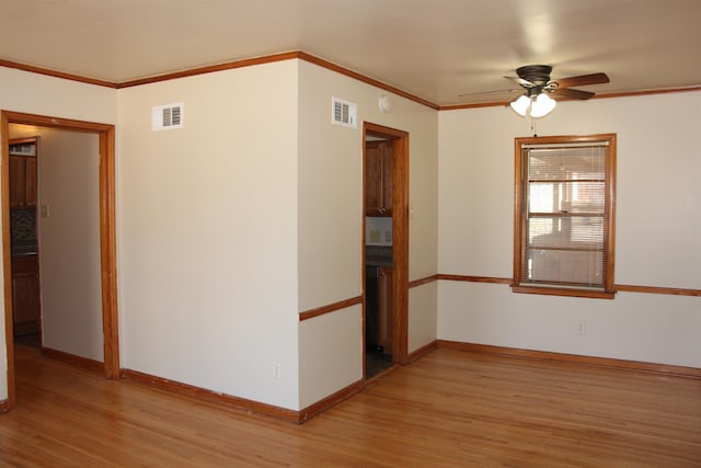 unfurnished room with light wood-style floors, baseboards, visible vents, and crown molding