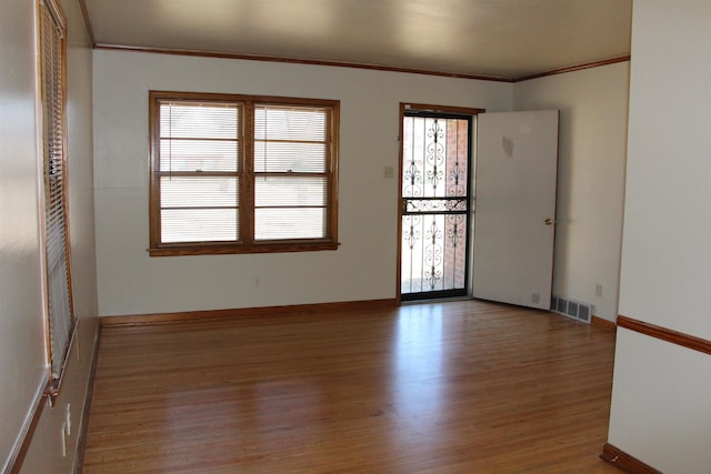 spare room featuring visible vents, crown molding, baseboards, and wood finished floors