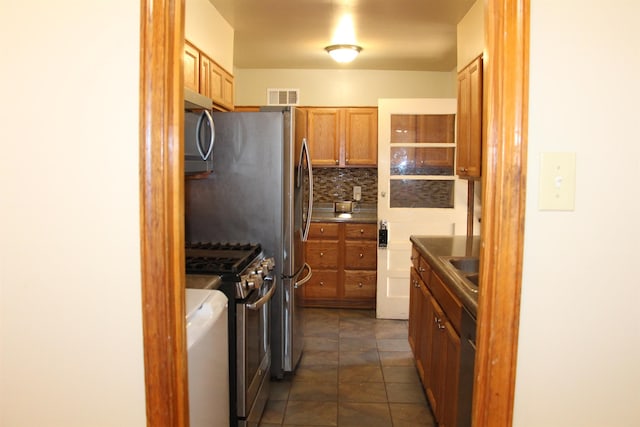 kitchen featuring visible vents, brown cabinetry, dark countertops, appliances with stainless steel finishes, and backsplash