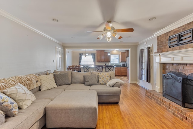 living area featuring ornamental molding, a fireplace, ceiling fan, and light wood-style flooring