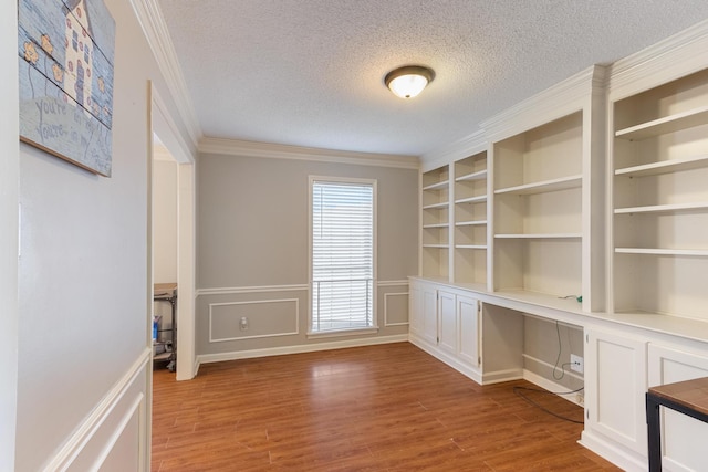 unfurnished office with a textured ceiling, wood finished floors, built in study area, and crown molding