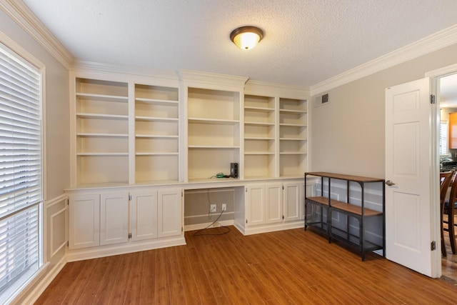 unfurnished office with crown molding, visible vents, built in study area, a textured ceiling, and wood finished floors