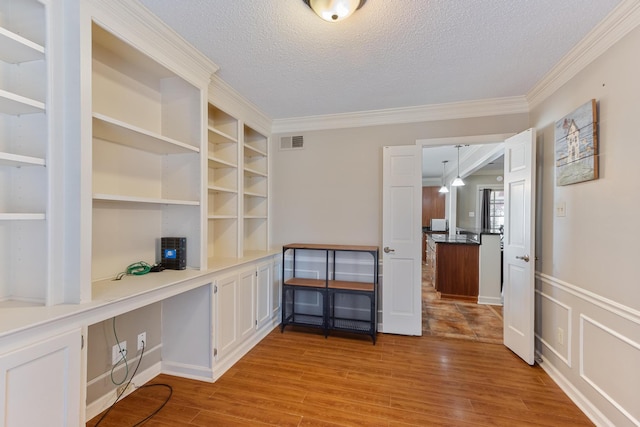 unfurnished office with visible vents, built in study area, ornamental molding, wood finished floors, and a textured ceiling