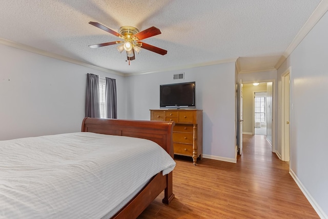 bedroom with baseboards, visible vents, ornamental molding, wood finished floors, and a textured ceiling