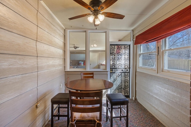 dining space featuring ceiling fan, carpet floors, and wood walls