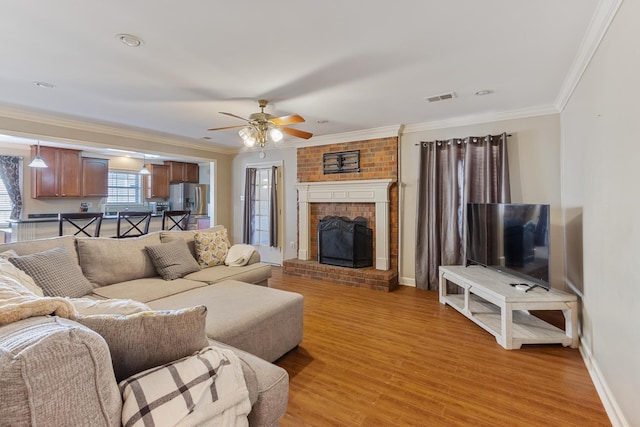 living room with crown molding, light wood finished floors, visible vents, a brick fireplace, and baseboards