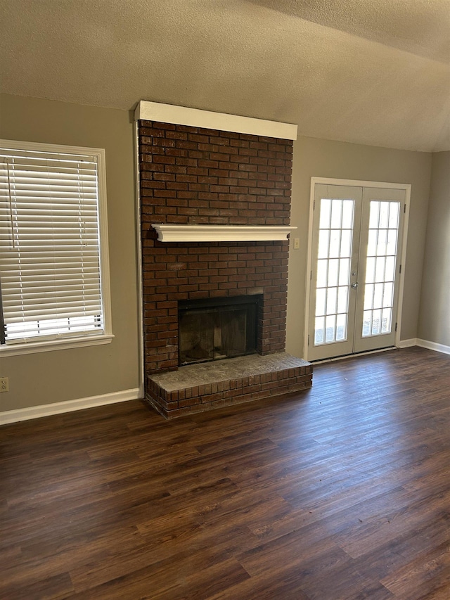 unfurnished living room with a textured ceiling, dark wood-style flooring, baseboards, french doors, and a brick fireplace