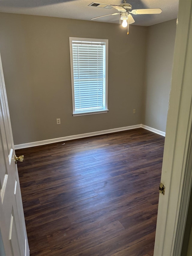 empty room featuring a textured ceiling, baseboards, dark wood-type flooring, and a ceiling fan