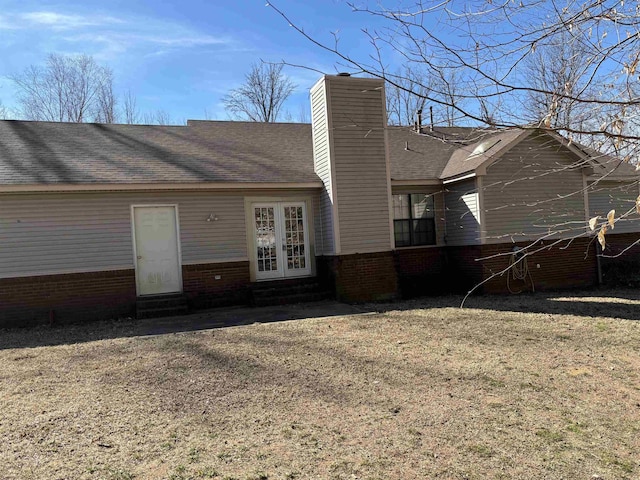 rear view of house with entry steps, a shingled roof, a chimney, french doors, and brick siding