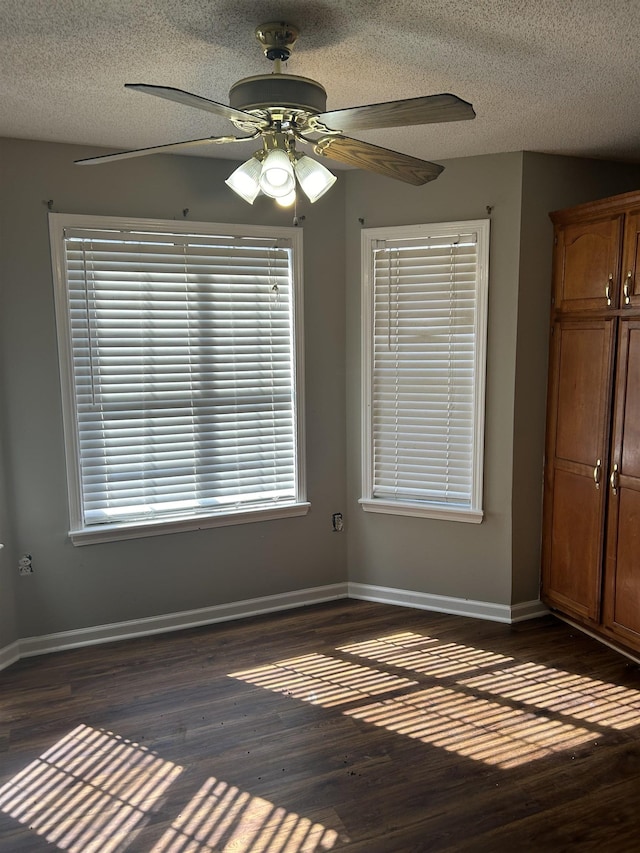 empty room with dark wood-style floors, ceiling fan, a textured ceiling, and baseboards