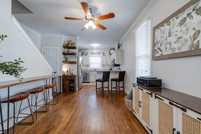 kitchen with dark wood-style flooring, appliances with stainless steel finishes, a kitchen breakfast bar, and crown molding