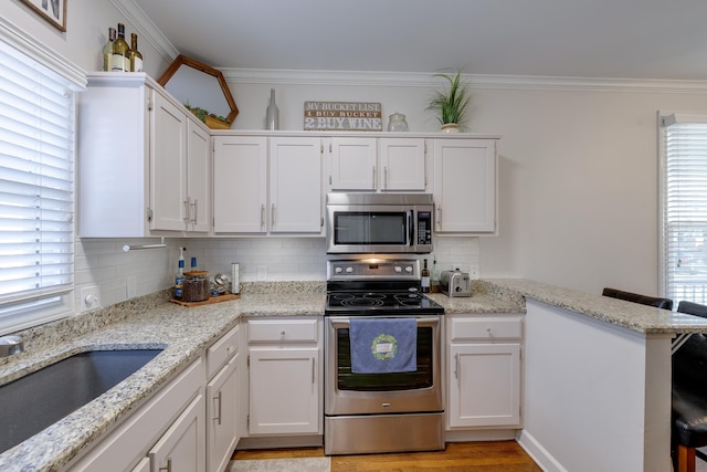 kitchen with stainless steel appliances, a sink, white cabinetry, and crown molding