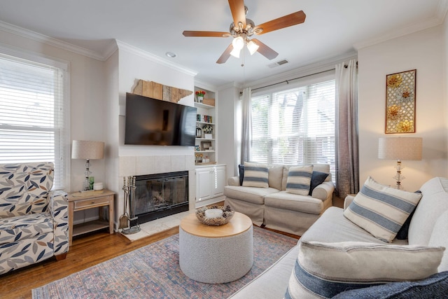 living area featuring built in shelves, crown molding, visible vents, light wood-style floors, and a tile fireplace