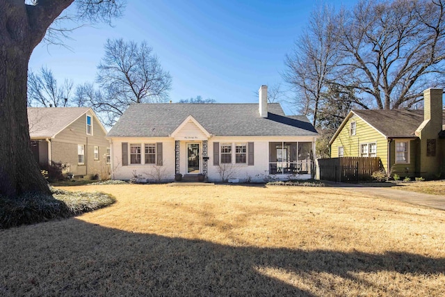 view of front facade featuring a sunroom, a chimney, roof with shingles, fence, and a front lawn