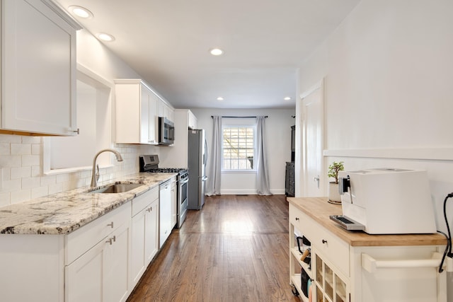 kitchen with stainless steel appliances, a sink, white cabinetry, backsplash, and dark wood-style floors