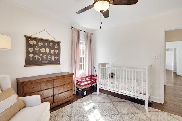 bedroom with ornamental molding, a ceiling fan, wood finished floors, a nursery area, and baseboards