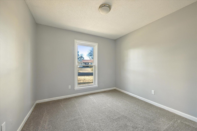 carpeted empty room featuring a textured ceiling and baseboards