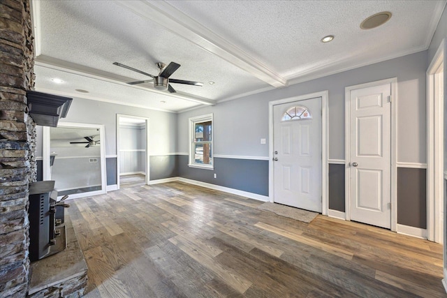 unfurnished living room featuring a ceiling fan, wood finished floors, a wood stove, crown molding, and a textured ceiling