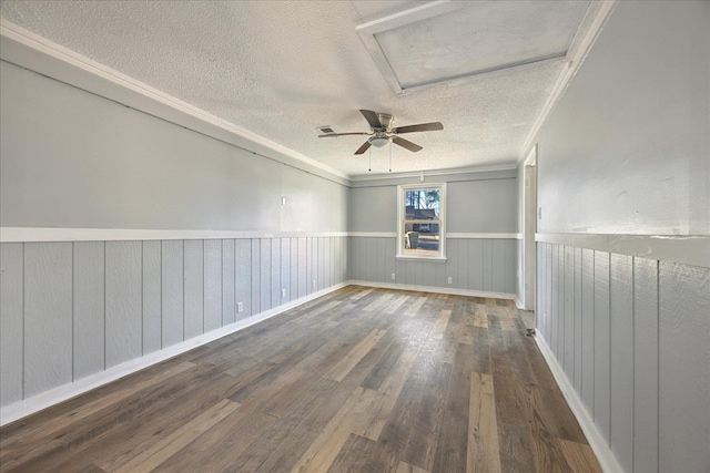 unfurnished room with a textured ceiling, a wainscoted wall, wood finished floors, ornamental molding, and attic access