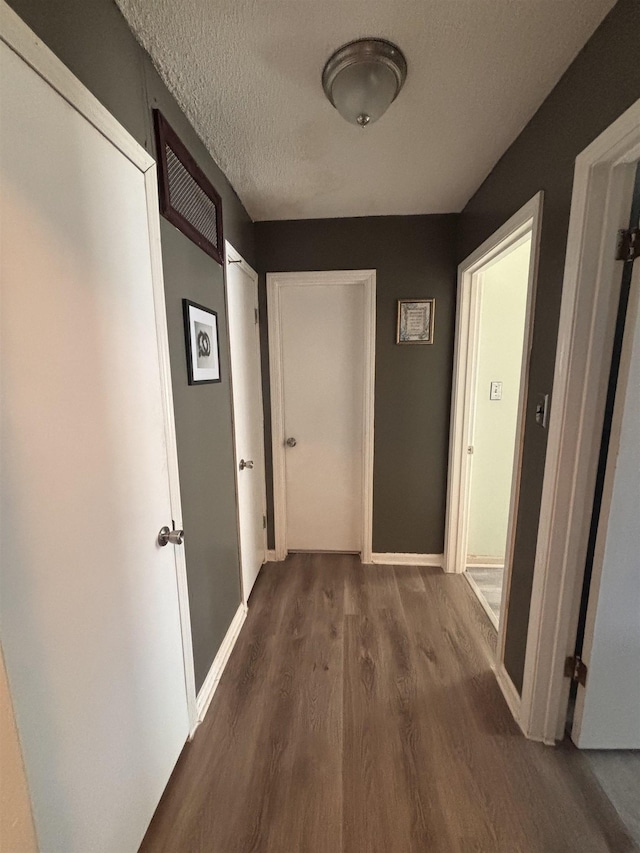 corridor featuring a textured ceiling, baseboards, and wood finished floors