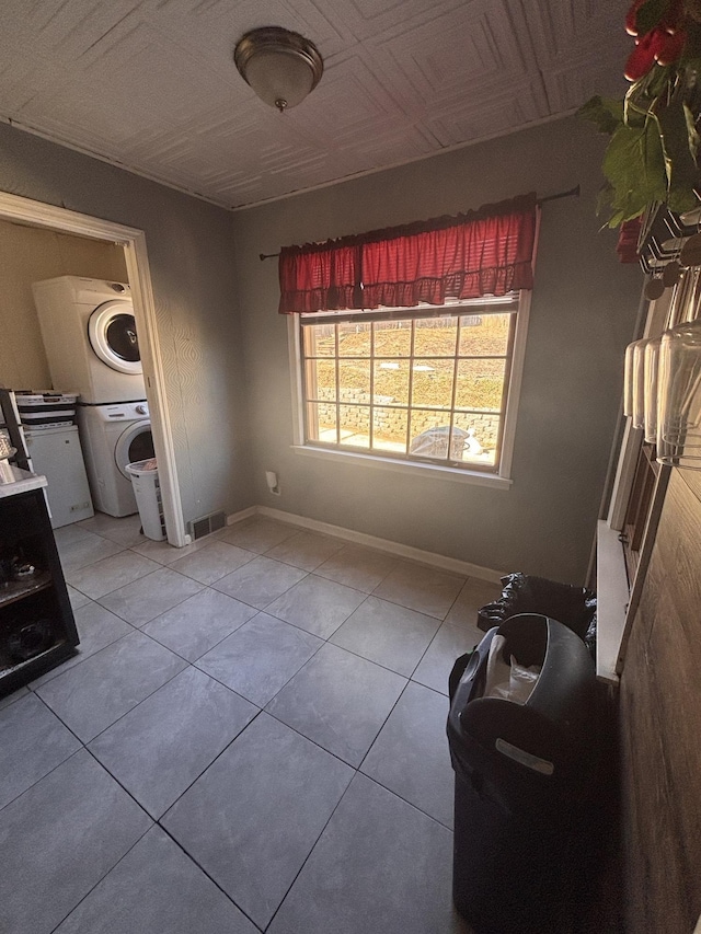 interior space featuring baseboards, visible vents, an ornate ceiling, tile patterned floors, and stacked washing maching and dryer