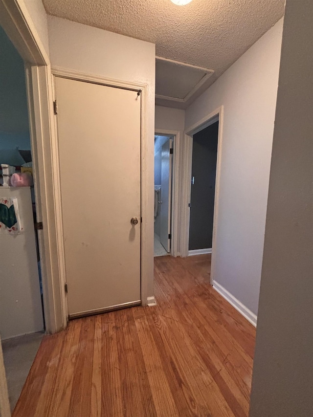 hallway featuring a textured ceiling, wood finished floors, and baseboards