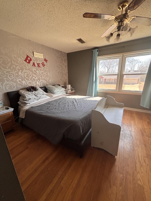 bedroom with wallpapered walls, visible vents, a ceiling fan, wood-type flooring, and a textured ceiling