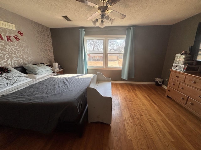 bedroom featuring light wood finished floors, baseboards, visible vents, ceiling fan, and a textured ceiling