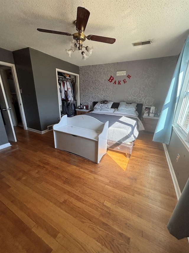 unfurnished bedroom with wallpapered walls, baseboards, visible vents, and wood finished floors