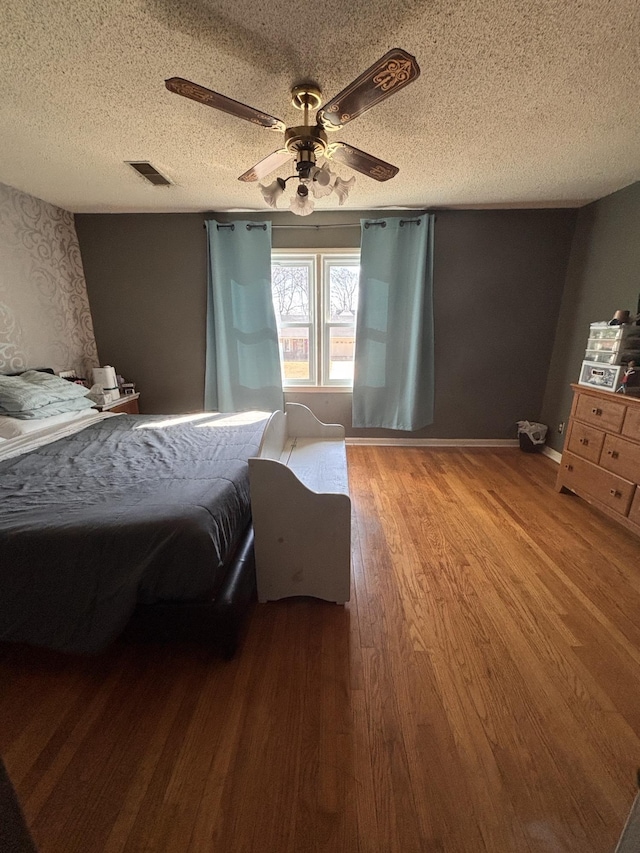 bedroom featuring visible vents, a textured ceiling, baseboards, and wood finished floors