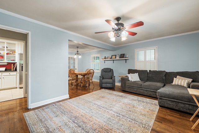 living area with ornamental molding, dark wood finished floors, a ceiling fan, and baseboards