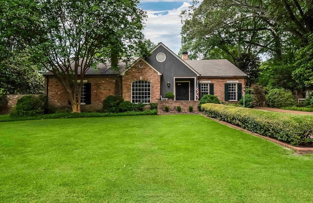 ranch-style home featuring brick siding, a chimney, and a front yard