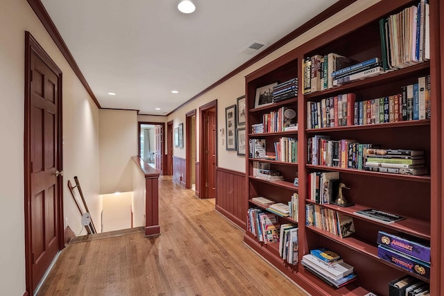 corridor with light wood-type flooring, wainscoting, ornamental molding, and an upstairs landing