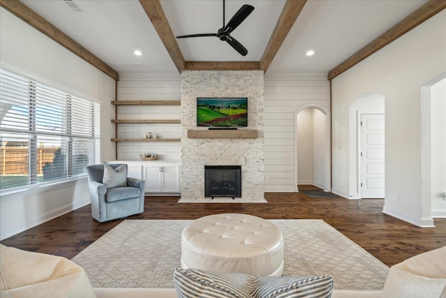 living room with arched walkways, ceiling fan, dark wood-style flooring, a fireplace, and beam ceiling