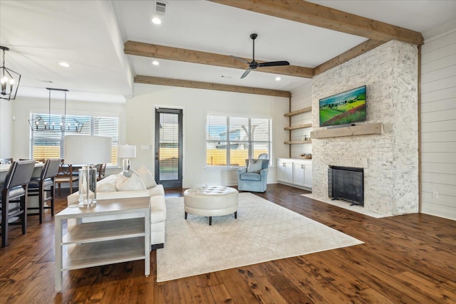 living area featuring visible vents, beamed ceiling, dark wood-type flooring, and a stone fireplace