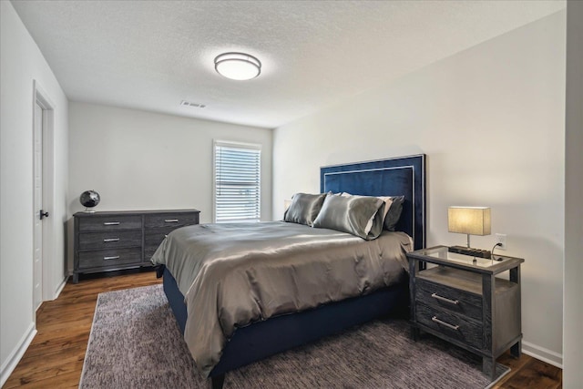 bedroom with dark wood-style floors, baseboards, visible vents, and a textured ceiling