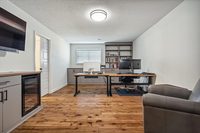 office area with light wood-style floors, wine cooler, a textured ceiling, and baseboards