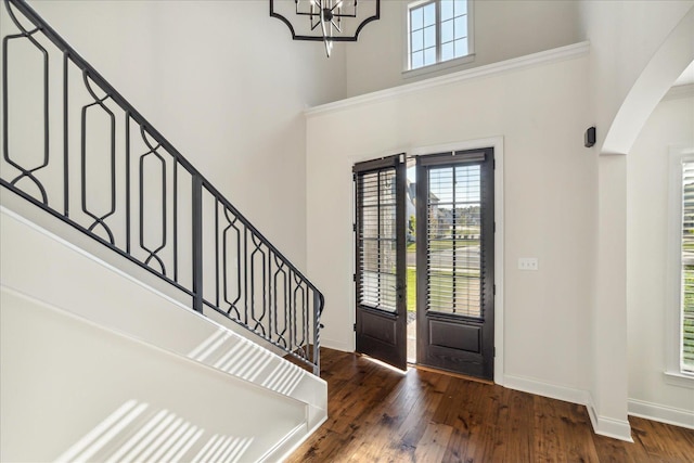 entryway with plenty of natural light, wood-type flooring, a towering ceiling, and baseboards