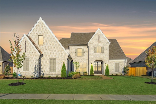 view of front of house with brick siding, a lawn, fence, and central air condition unit