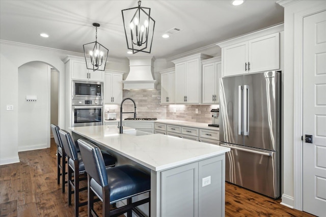 kitchen featuring arched walkways, a sink, visible vents, appliances with stainless steel finishes, and custom exhaust hood