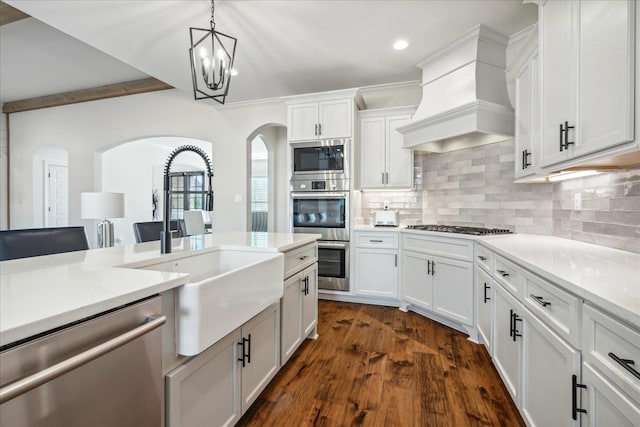 kitchen with arched walkways, stainless steel appliances, a sink, backsplash, and custom range hood