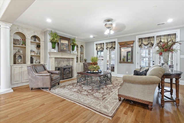 living area featuring a fireplace, crown molding, visible vents, light wood-style floors, and ornate columns