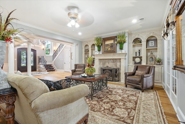 living room with decorative columns, light wood-style flooring, a premium fireplace, ornamental molding, and stairs