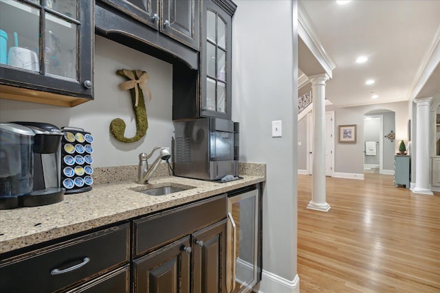 kitchen featuring beverage cooler, decorative columns, ornamental molding, light wood-style floors, and a sink